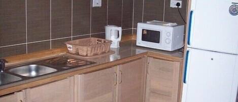 Una cocina con armarios de madera, microondas, hervidor y estufa.