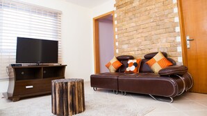 Een woonkamer met een flatscreen televisie, een houten salontafel, een leren bank met gestreepte kussens en een accentmuur van baksteen.