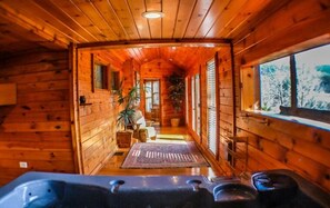 A wooden cabin interior with a hot tub, a rug, and a window with a view of trees. - Jordan Lodge (Blue Ridge)