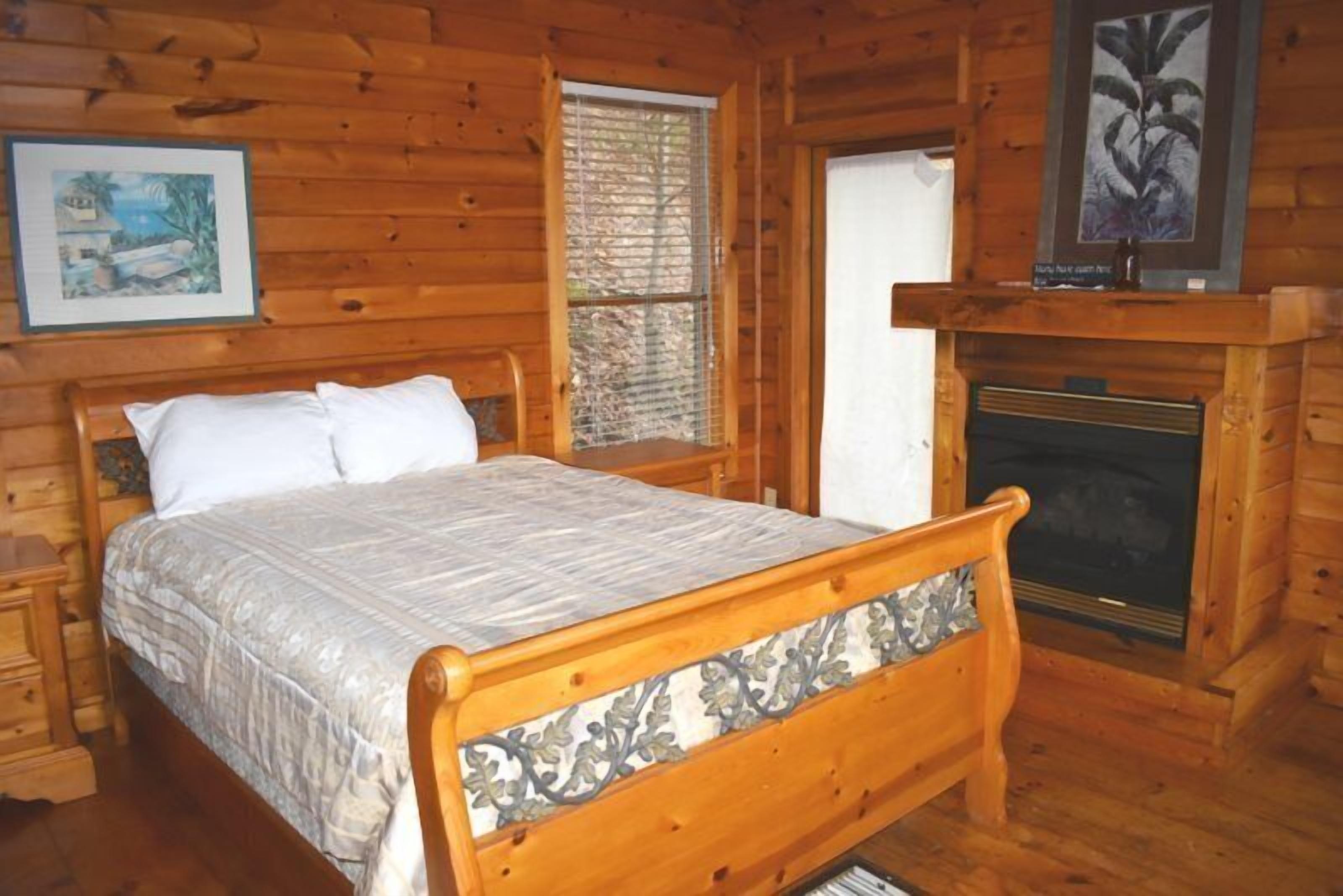 A wooden cabin bedroom with a bed, a fireplace, and a window with blinds.