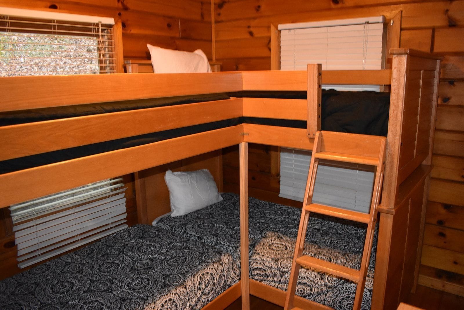 Une chambre avec un lit superposé, une échelle, une fenêtre avec des stores et un tapis à motifs.