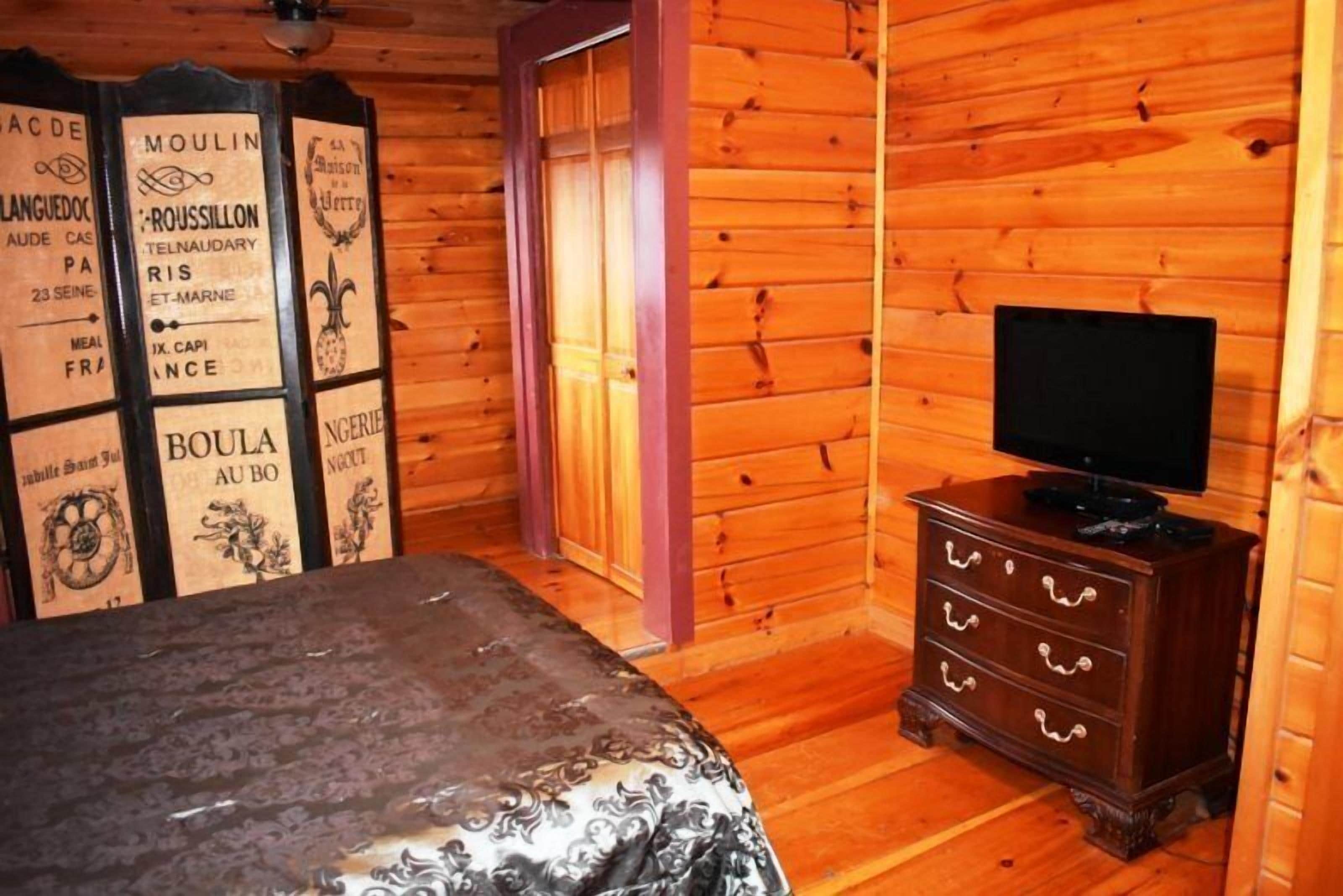 Una habitación con paneles de madera, una cama, un aparador con televisor y decoraciones de estilo vintage.