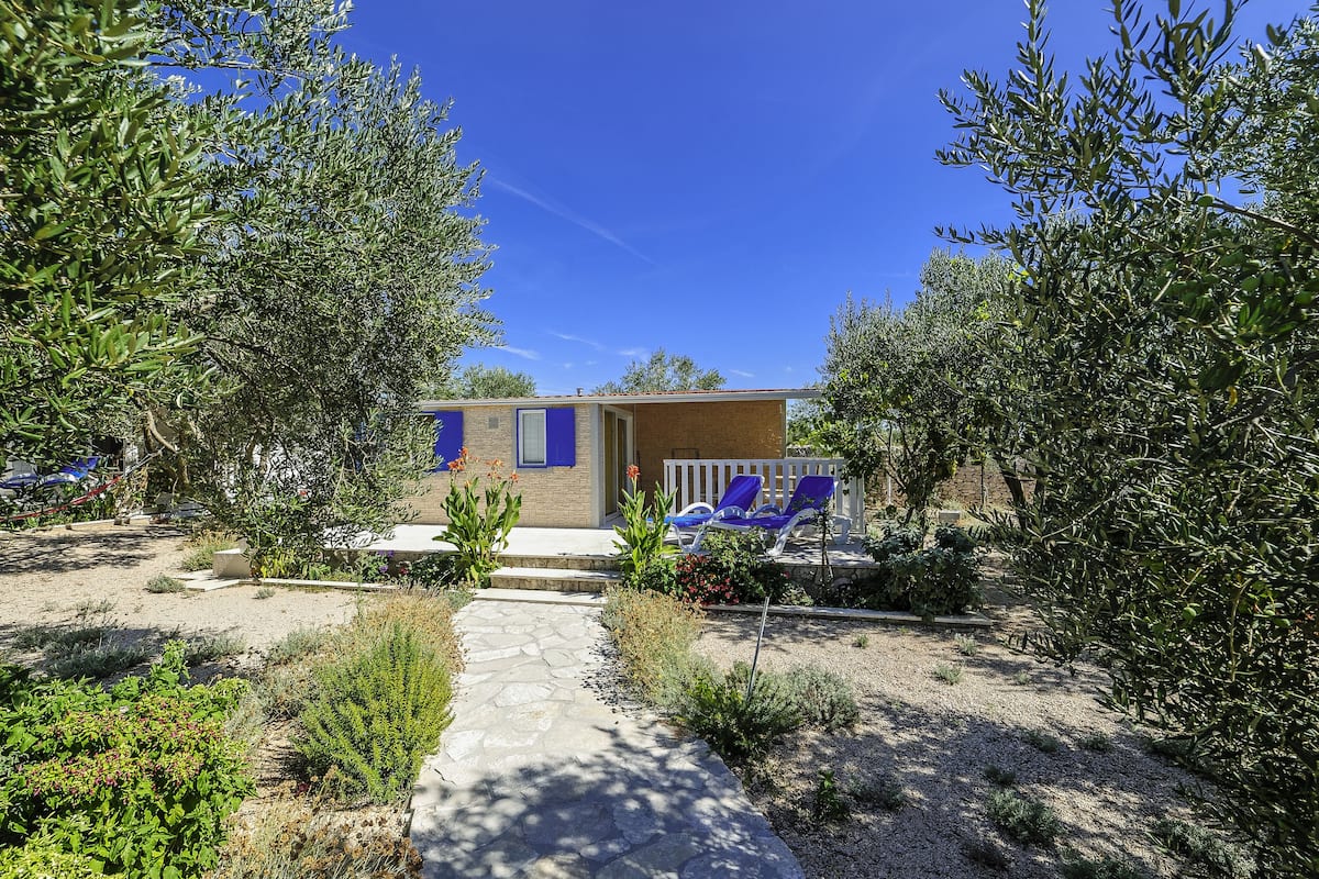 Une petite maison avec un chemin de pierres menant à un porche où se trouvent des chaises bleues.