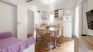 A compact room with a bed, a dining table with chairs, a kitchenette, and a TV. - Olive Garden Camp Resort (Sibenik)