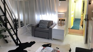 A modern living room with a sofa, a coffee table, and a lamp. There is a staircase with a wooden railing and a plant. - A5G Skyglass (París)