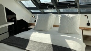 A modern hotel room with a skylight, a bed with white linens, a bedside table, and a wall-mounted lamp. - A5G Skyglass (París)