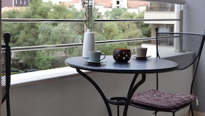 A balcony with a table and chairs, a vase with plants, and a view of a hillside with buildings. - Yeshill Apartments (Budva)