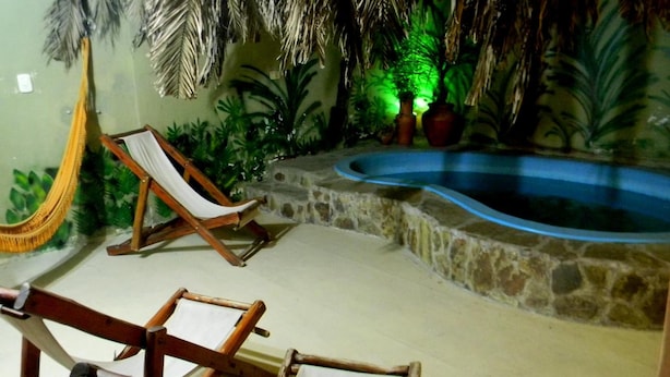 A pool area with a stone wall, a hammock, and two wooden lounge chairs. - Jujuy Hostel (San Salvador de Jujuy)