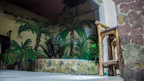 A room with a stone wall, a wooden chair, and a mural of palm trees. - Jujuy Hostel (San Salvador de Jujuy)