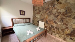A bedroom with a stone wall, a wooden bed frame, a green bedspread, and a hanging light fixture. - Jujuy Hostel (San Salvador de Jujuy)