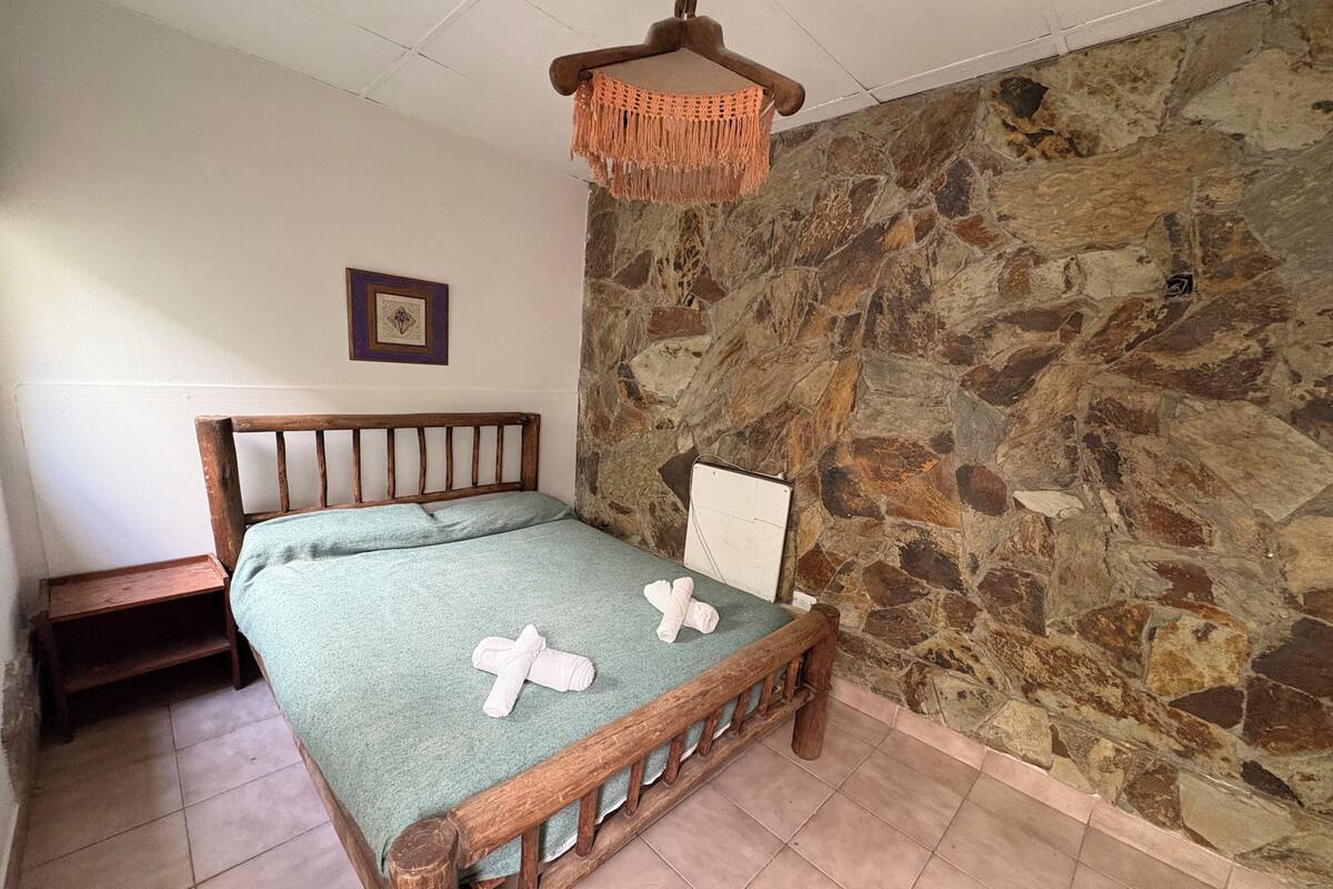 Ein Schlafzimmer mit einer Steinsandsteinwand, einem Holzbettgestell, einer grünen Bettdecke und einer Pendelleuchte.