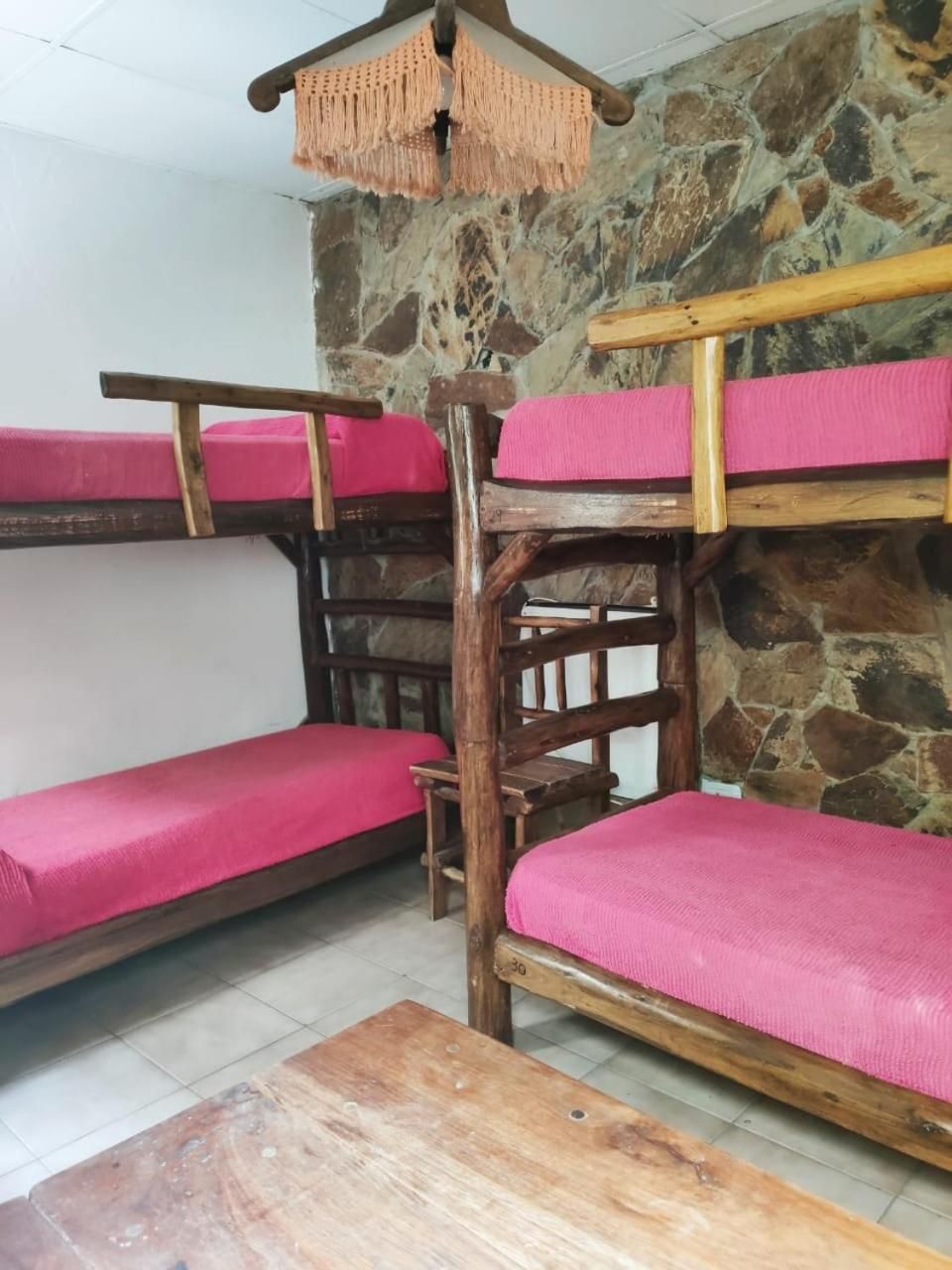 Una cama litera con ropa de cama rosa, una mesa de madera y una pared de piedra.