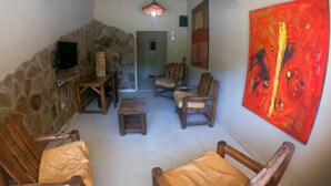 A cozy living room with stone walls, wooden furniture, a television, and a large abstract painting. - Jujuy Hostel (San Salvador de Jujuy)