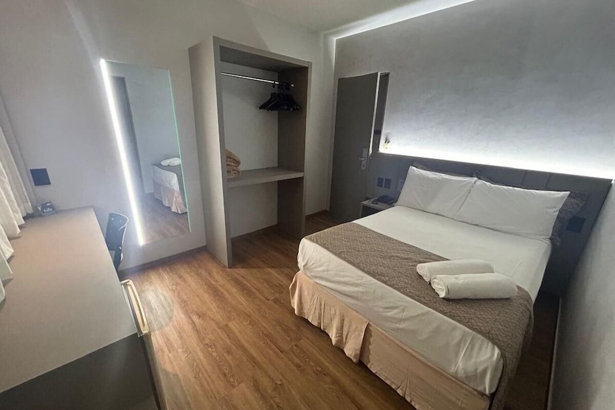 A modern hotel room with a bed, a built-in closet, and a bedside table.
