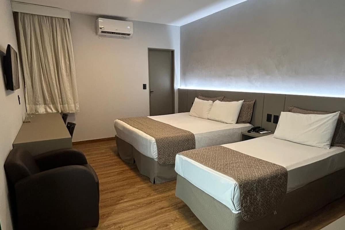 A hotel room with two beds, a desk, a chair, and an air conditioning unit.