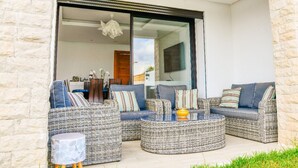 A modern outdoor seating area with wicker furniture and a glass door leading to an interior space. - GREAT VILLA OF NATIONS (BOUKNADEL)