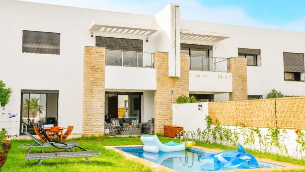 A modern two-story building with a swimming pool, outdoor seating, and a stone wall. - GREAT VILLA OF NATIONS (BOUKNADEL)