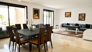 A modern living room with a dining table and chairs, a sofa, and artwork on the walls. - GREAT VILLA OF NATIONS (BOUKNADEL)