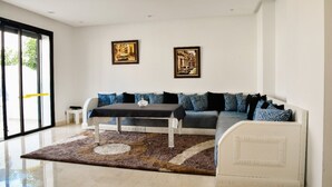 A modern living room with a sofa, a coffee table, and two framed pictures on the wall. - GREAT VILLA OF NATIONS (BOUKNADEL)