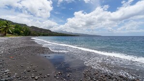 A beach with dark pebbles, calm water, and a clear sky.