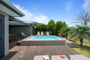 Ein Swimmingpool mit Liegestühlen, einer Holzterrasse und einem Gebäude mit grauer Fassade.