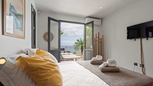 A bedroom with a bed, a bedside table with towels, a TV, and a view of the sea.