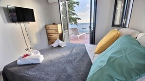 A bedroom with a bed, a TV, a dresser, and a view of the sea.