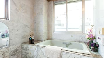 A bathroom with a marble floor, a bathtub, a large mirror, and a window.