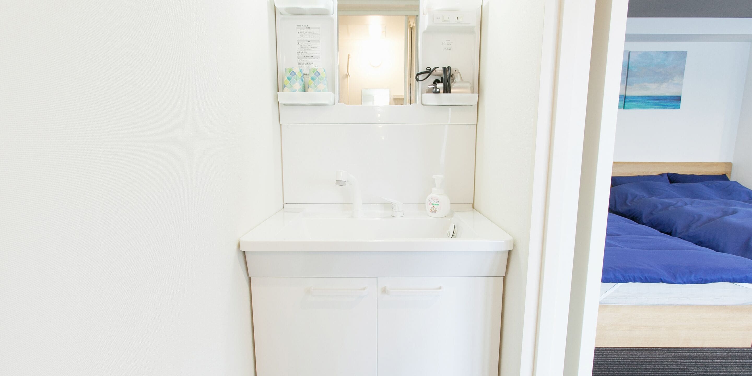Une salle de bain d’hôtel avec un lavabo blanc, un miroir et un meuble de rangement.