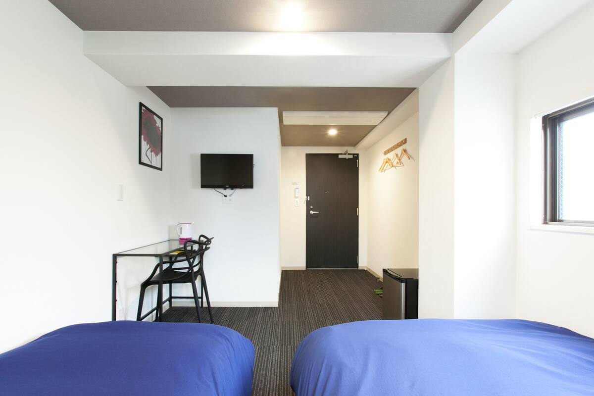A hotel room with two beds, a desk with a chair, a television, and a door leading to another room.