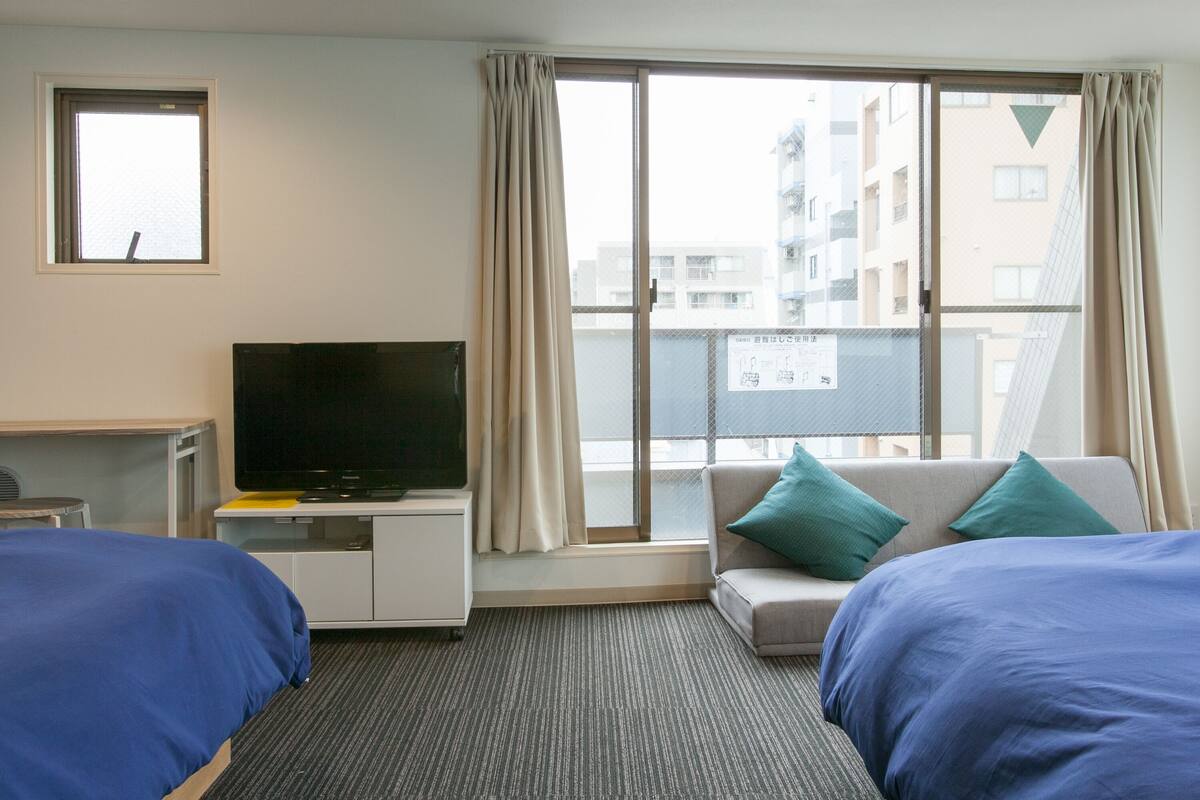 A hotel room with two beds, a TV, a desk, and a window with curtains.