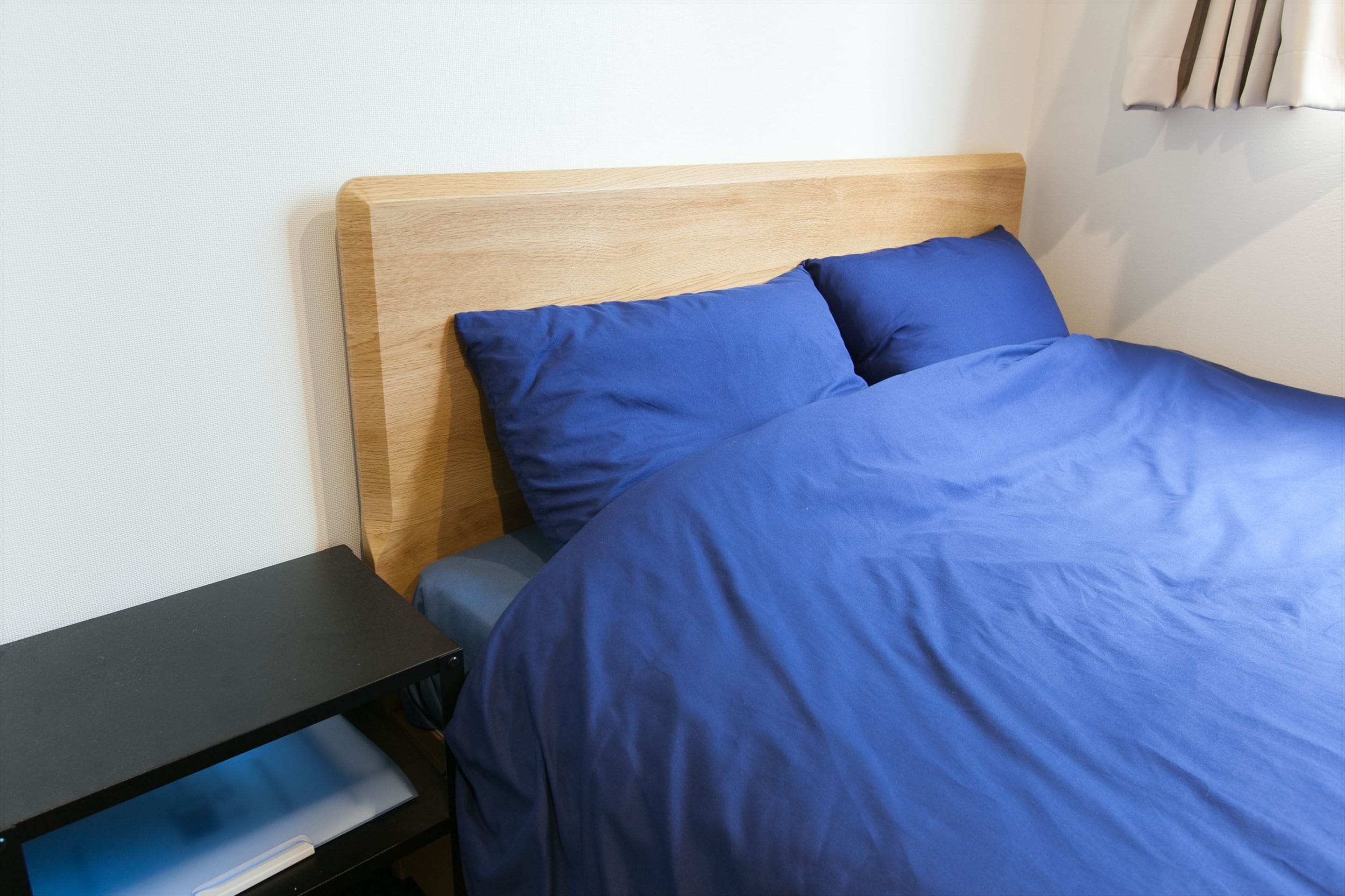 A neatly made bed with blue bedding, a wooden headboard, and a black nightstand with a drawer.