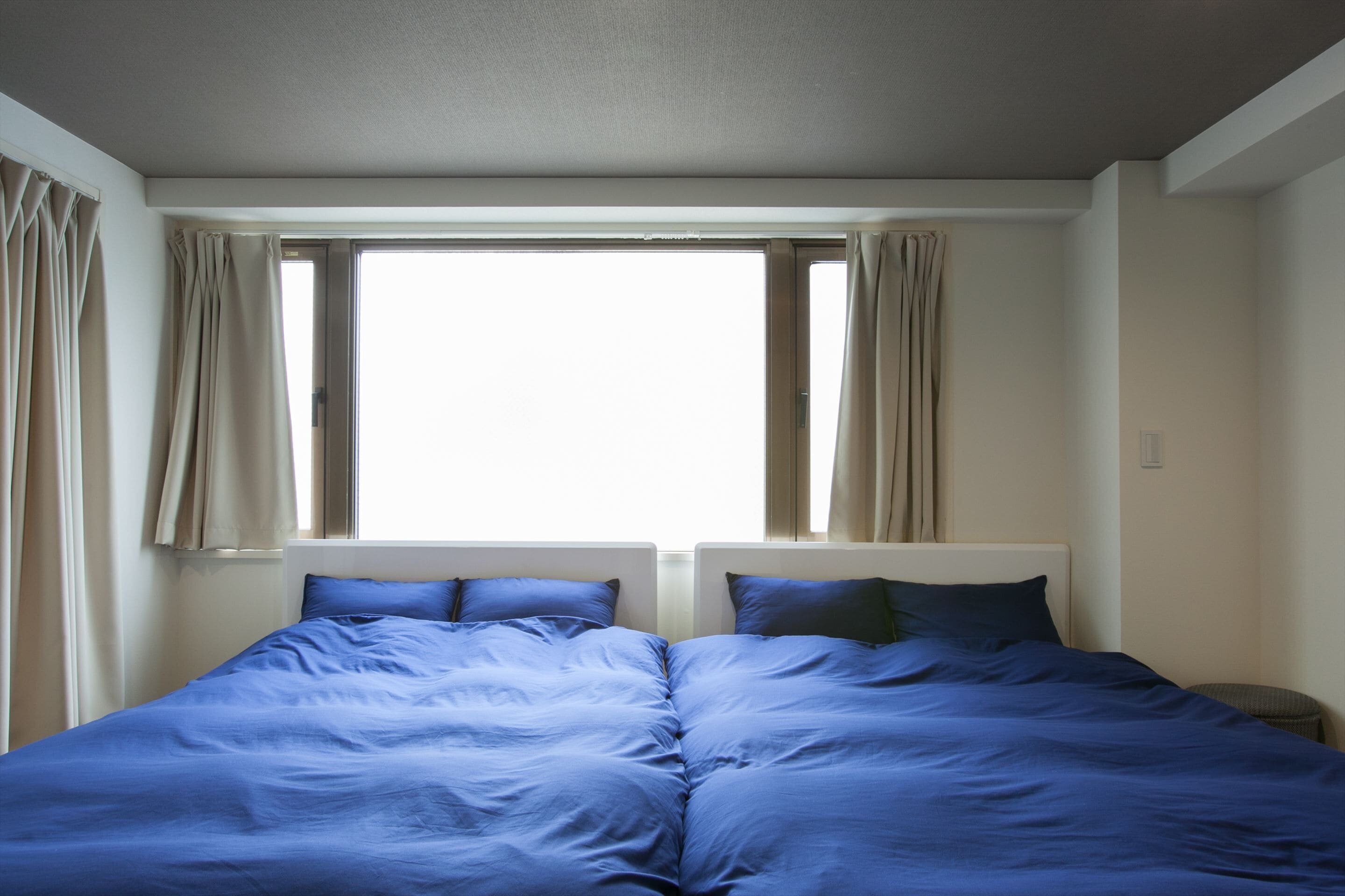 Cama doble con ropa de cama azul en una habitación con un ventanal y cortinas.