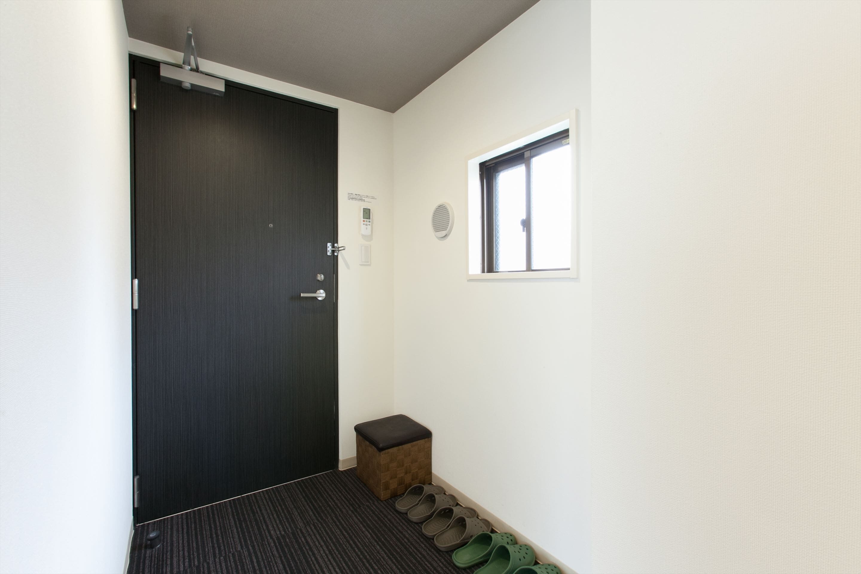A hallway with a dark wooden door, a small stool, and a window with blinds.