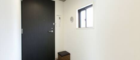 A hallway with a dark wooden door, a small stool, and a window with blinds.