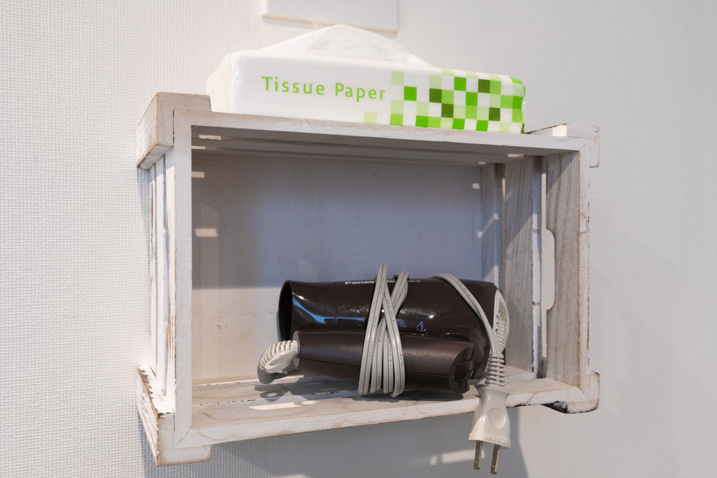 En lille, hvid, vintage-stil æske med teksten 'Tissue Paper' på en muret væg.