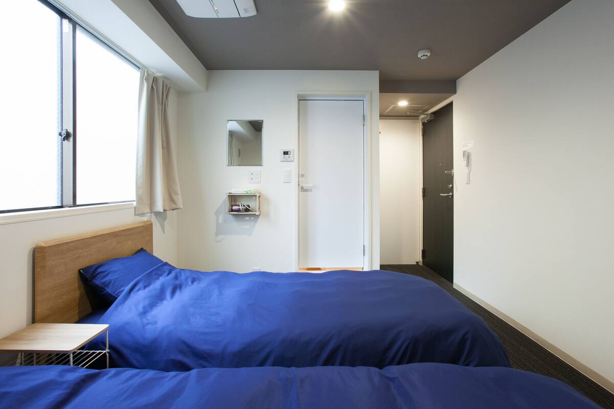 A hotel room with a large bed, a bedside table, a window with curtains, a door, and a small mirror on the wall.