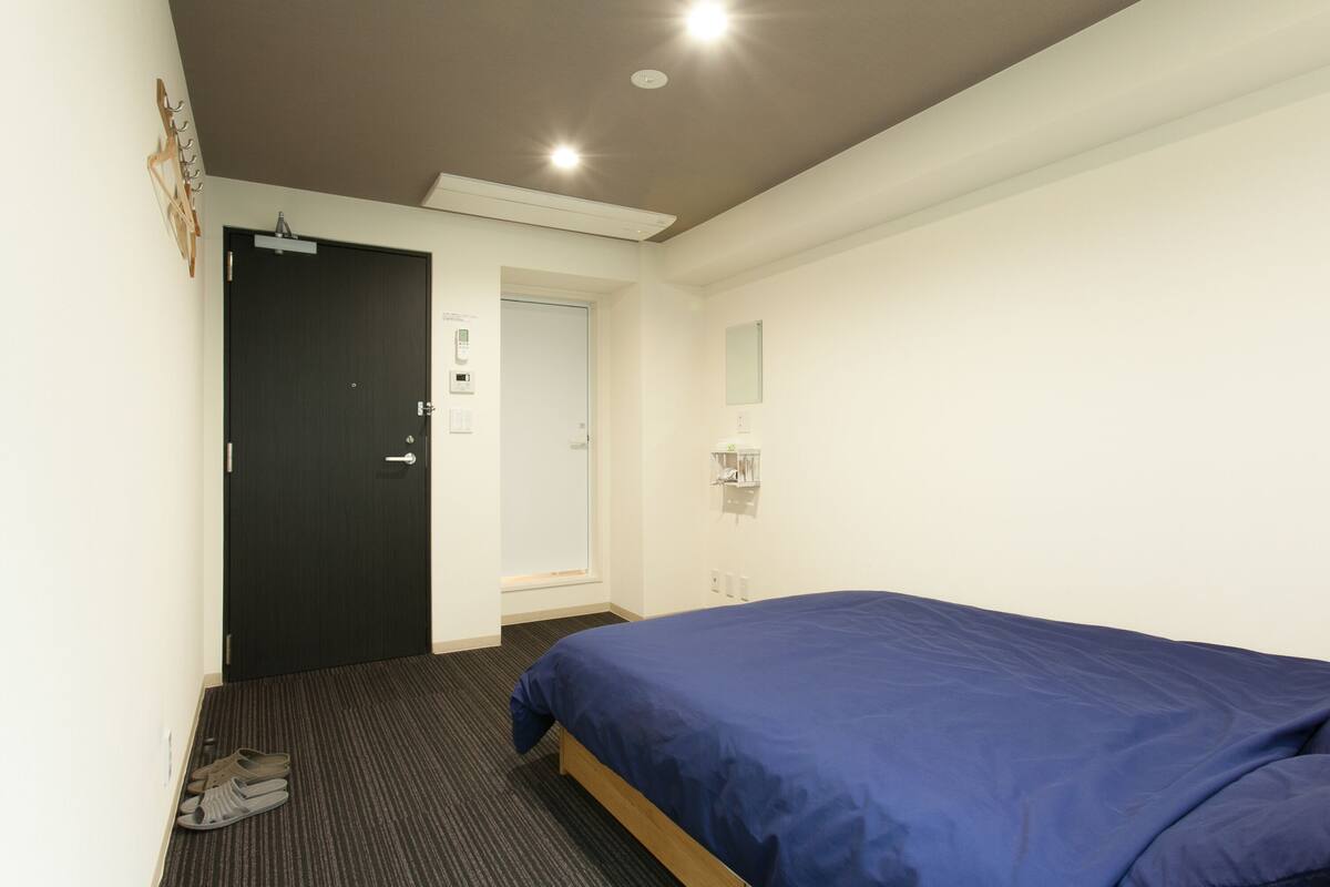 A bedroom with a bed, a door, a shoe rack, and a mirror.
