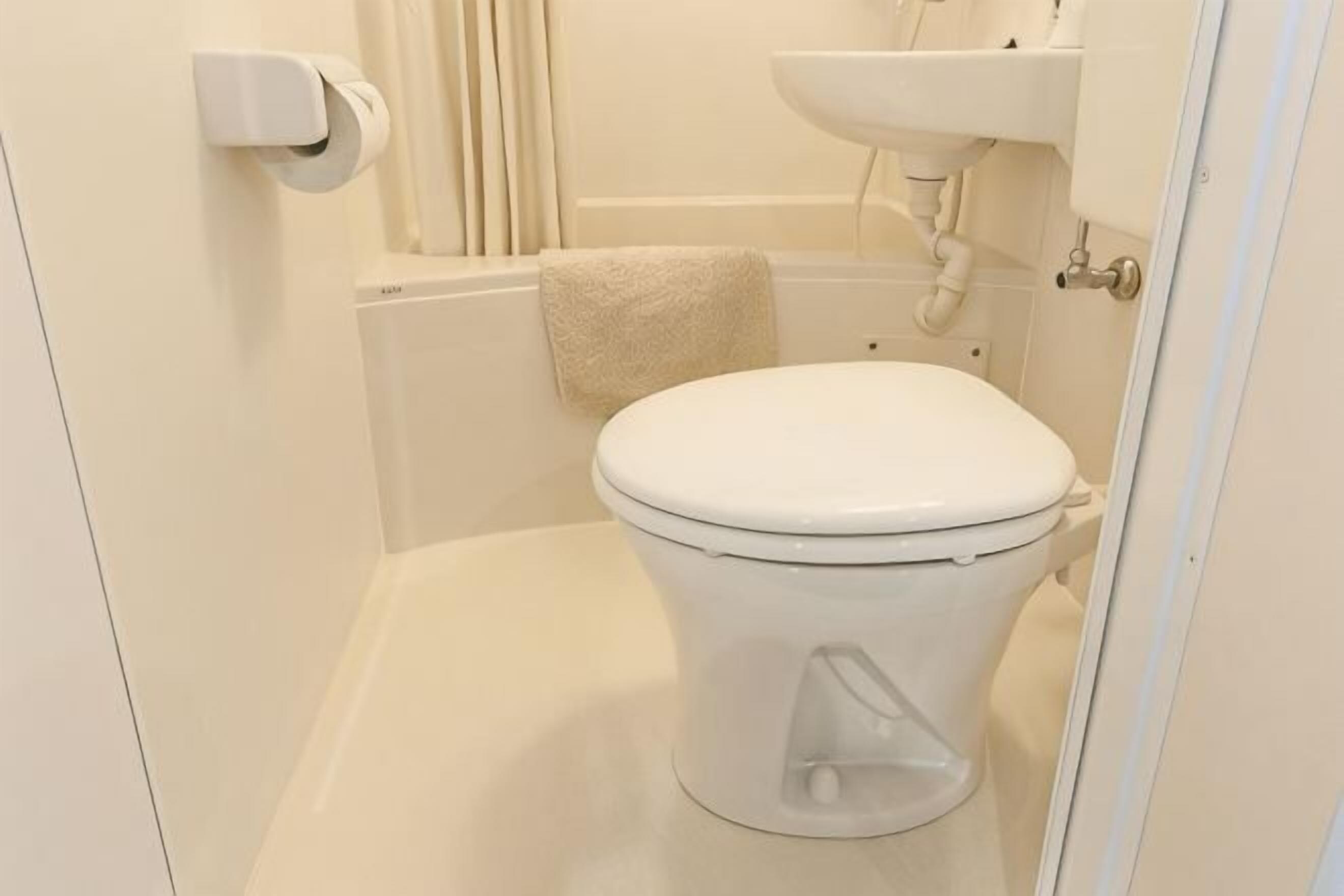 A small, white toilet in a bathroom with a white sink and towel hanging on the wall.