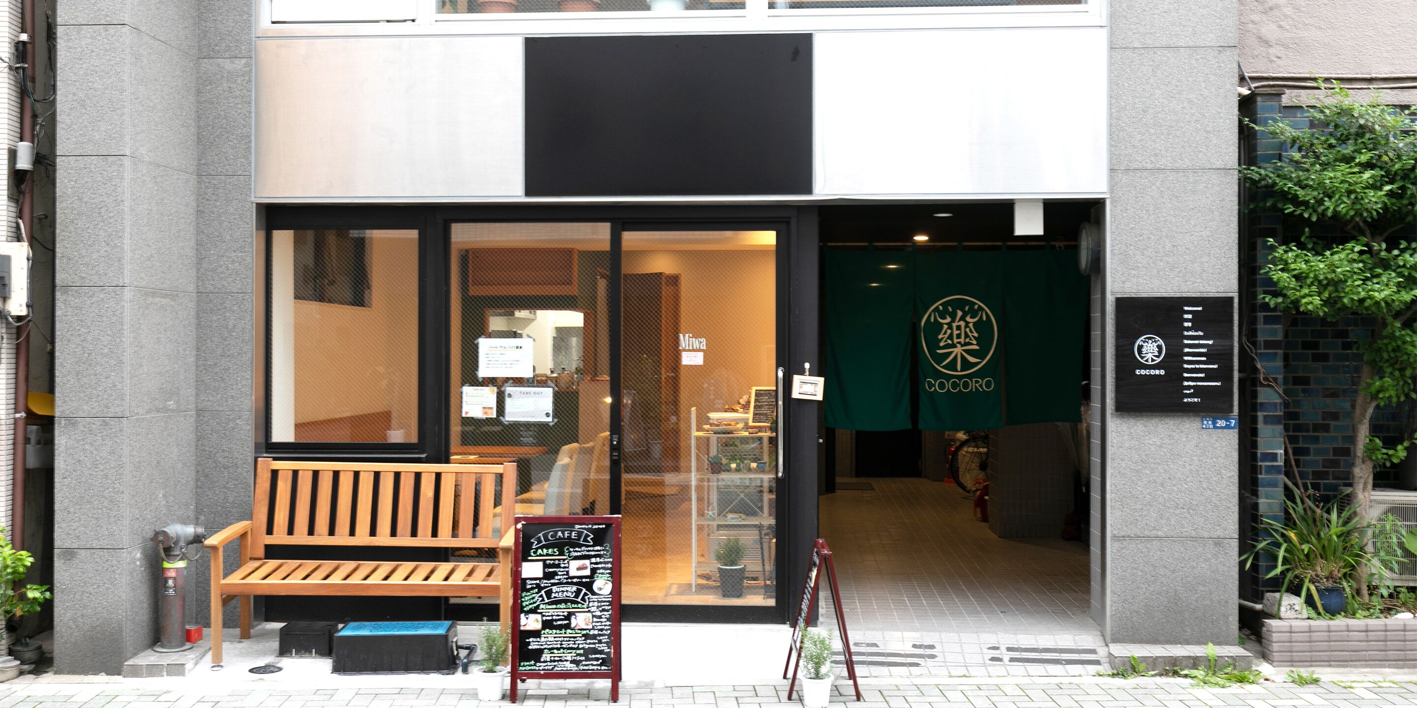 A cafe with a wooden bench outside, a menu board, and a green sign with gold lettering.