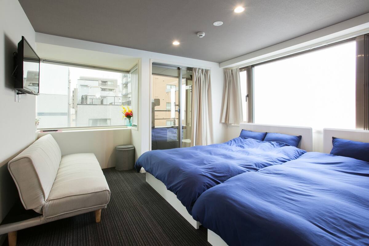A hotel room with a bed, a sofa, a TV, and a window with curtains.