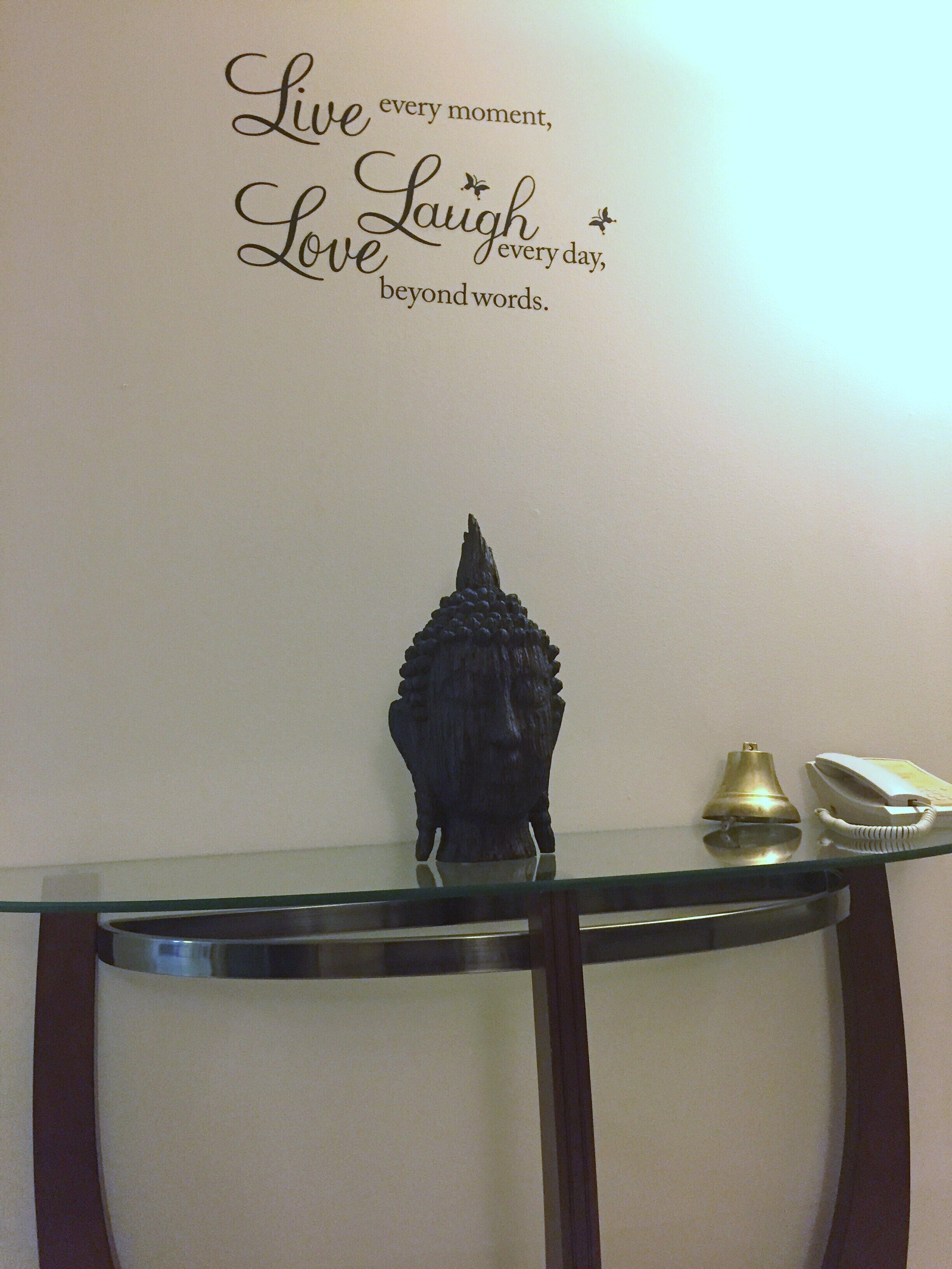 Un mur orné d’une citation inspirante et une statue de Bouddha décorative posée sur une table en verre.