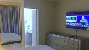 A hotel room with a bed, a dresser, a television displaying news, and a door leading to a bathroom. - DISCOUNTED Royal Islander Club 2 Bdrm Suite, Sleeps 6, Wifi, Pool, - MAHO BEACH! (Maho Bay)