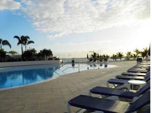 Un área de piscina con sillones de descanso y palmeras.