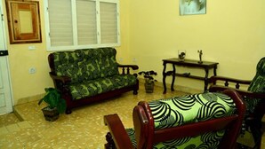 Una sala de estar con un sofá, una silla de madera, una mesita y una planta en maceta.