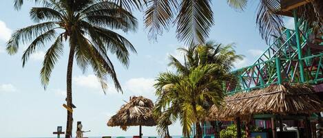 A beach with palm trees, a thatched-roof structure, and colorful lounge chairs.