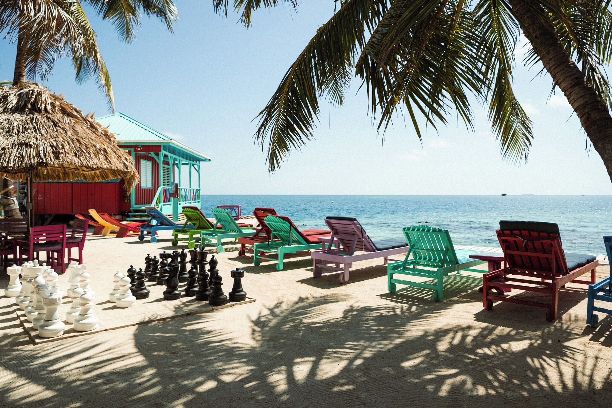 A beach with colorful lounge chairs, a thatched-roof building, and a clear view of the sea.