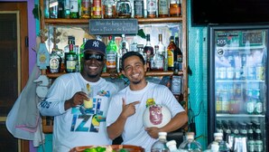 Two men standing in front of a bar with various bottles and a sign that reads "When the King is happy there is Peace in the Kingdom." - King Lewey's Island Resort (Placencia)