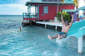 Une personne glisse dans une eau turquoise depuis un toboggan fixé à un bâtiment rouge doté d’une véranda.