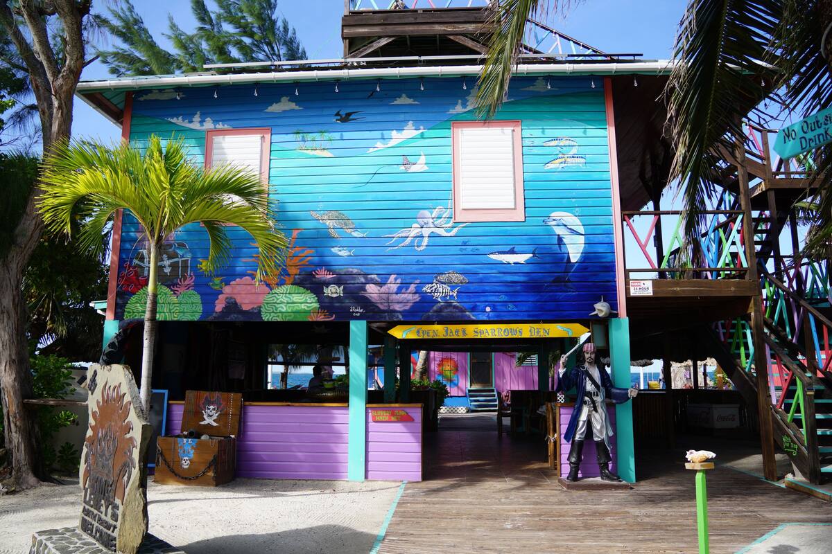 Um edifício colorido com um mural de vida marinha, uma placa com a inscrição 'No Out of State Drink' e uma estátua de pirata.